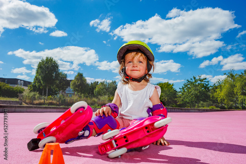 Girl learn rollers, sit in protection on color floor of the park photo