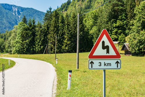 Triangular white and red road sign of winding roads ahead, mountain road with series of dangerous curves for three kilometers. Julian Alps, Triglav National Park, Slovenia, central Europe.