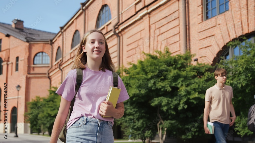 Cheerful teenage girl with books and backpack walk outside school building Cheerful teenage girl with books and backpack walk outside school building