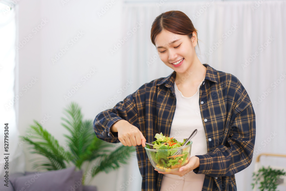 Lifestyle in living room concept, Young Asian woman standing to mixing vegetable salad in bowl Lifestyle in living room concept, Young Asian woman standing to mixing vegetable salad in bowl