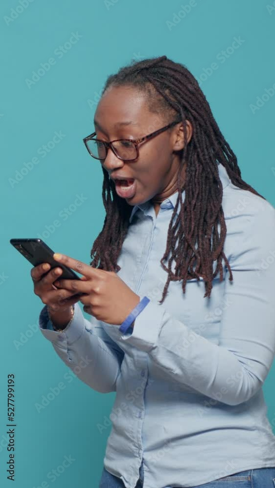 Vertical video: Happy excited model using online app on smartphone, browsing social media internet website and feeling positive about text messages. Cheerful smiling person showing excitement in Vertical video: Happy excited model using online app on smartphone, browsing social media internet website and feeling positive about text messages. Cheerful smiling person showing excitement in