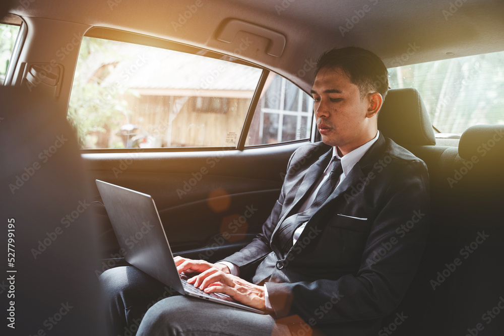 Young Asian businessman using a laptop in the backseat of a car.