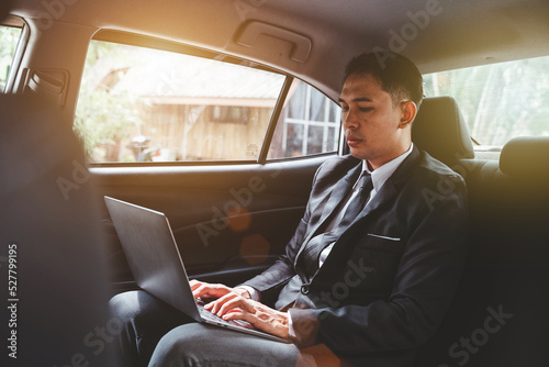 Young Asian businessman using a laptop in the backseat of a car. © makibestphoto