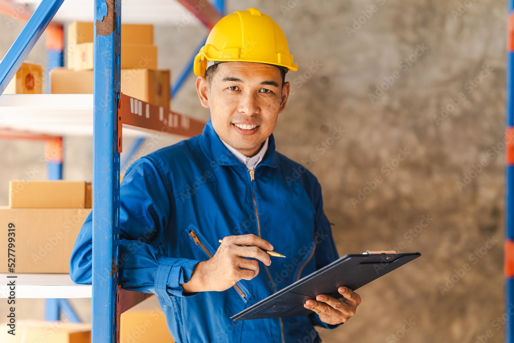 Fototapeta premium Business Asian warehouse worker checking packages in storehouse and holding paper clipboard.