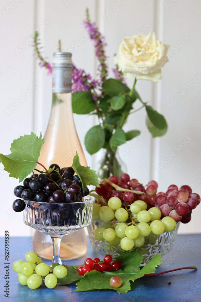 Still life with wine and grapes. Colorful photo of bottle of rose wine and different sorts of grapes. Seasonal fruit on a table. 