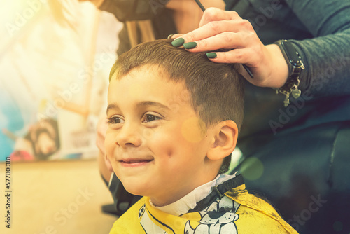 little boy having a haircut at hair salon..Children hairdresser with scissors and comb is cutting little boy. Contented cute preschooler boy getting the haircut. toned