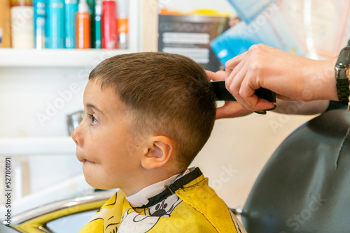 little boy having a haircut at hair salon..Children hairdresser with scissors and comb is cutting little boy. Contented cute preschooler boy getting the haircut