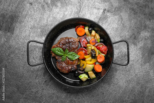 Pan with tasty steak and vegetables on grey table, top view
