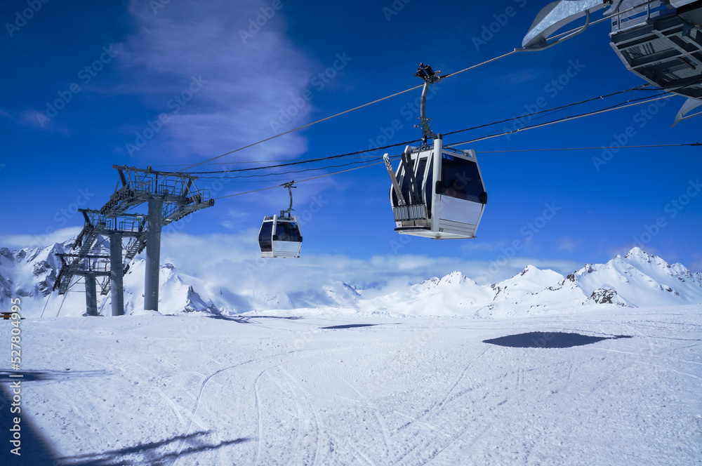 Obraz premium Funitel aerial lift in snow mountains against blue sky with clouds in bright winter day