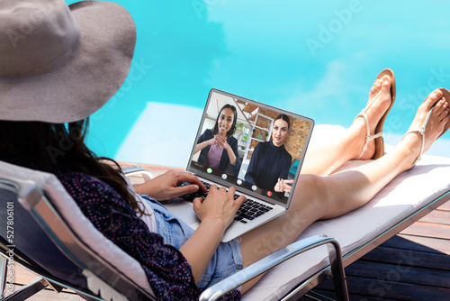 Rear view of woman having a video conference on laptop near the pool photo