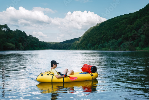 Tourist on yellow packraft rubber boat with red padle on a sunrise river. Packrafting. Active lifestile concept photo