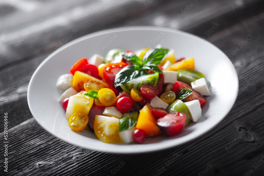 Salad with different varieties kind of red, yellow, green and black tomato mix, mozzarella cheese and basil. Caprese salas with fresh colourful tomatoes. Food photography
