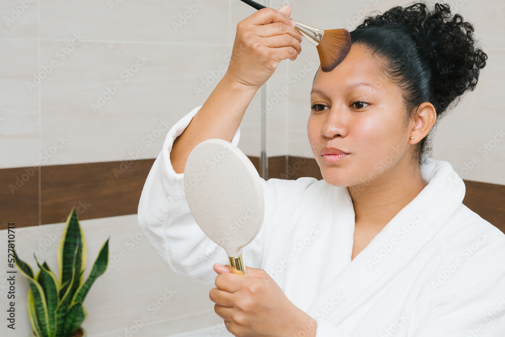 Content ethnic woman applying foundation on face