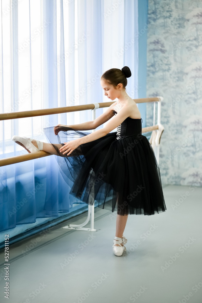 A beautiful girl ballerina in a black dress is engaged at the stonk. She's in a dance studio. Beauty. Dancing. Creation.