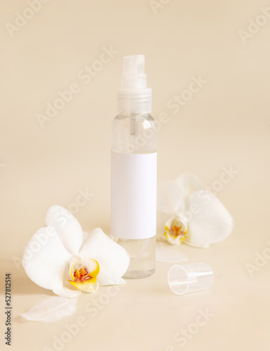 Spray dispenser bottle near white orchid flowers on light beige close up. Mockup