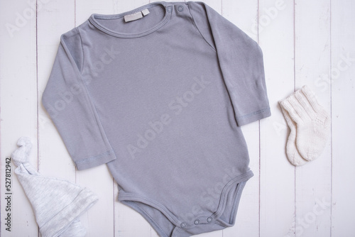 Grey baby bodysuit mockup for logo, text or design on wooden background with hat and socks top view © Alina
