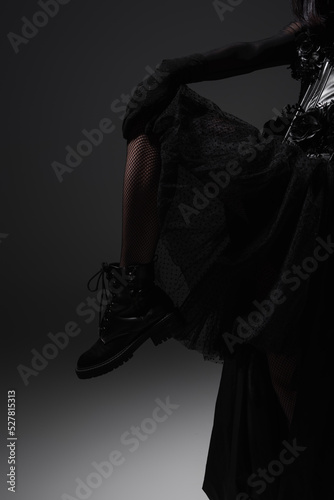 cropped view of woman in gothic dress and black boot posing on grey.