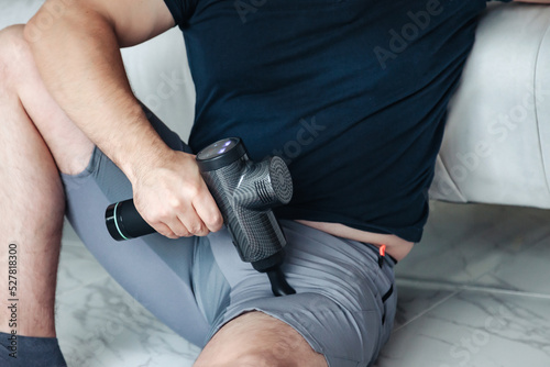 Gun shock vibration percussion massage therapy. Sporty man practicing self-massaging your hands close-up. Applying therapeutic percussive massage gun in living room at home indoors. Copy text space