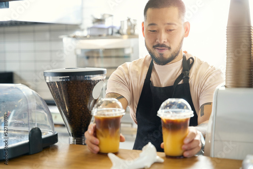 Lovely Asian coffee shop worker presenting two fresh iced beverages photo