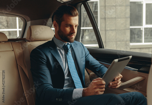 Seriously business man looking to the screen of modern device in auto © Friends Stock