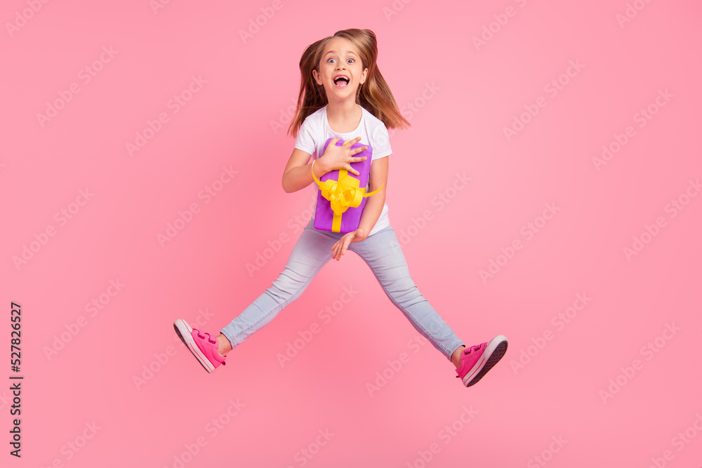 Full body photo of astonished energetic girl jump hands hold giftbox isolated on pink color background Full body photo of astonished energetic girl jump hands hold giftbox isolated on pink color background