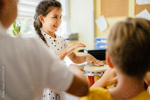 Canvas Print Cute little pupil girl play with drums at classroom Children with musical instruments at school