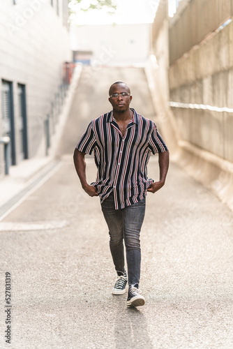 Chico negro joven rapado con camisa de rayas verticales posando en la calle