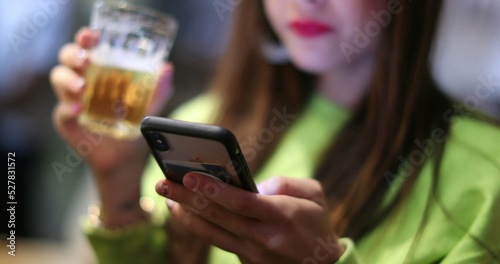 Woman holding beer looking at smartphone