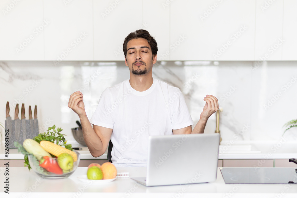 Young handsome vegetarian man meditating in the kitchen. Online training and food blogger concept Young handsome vegetarian man meditating in the kitchen. Online training and food blogger concept