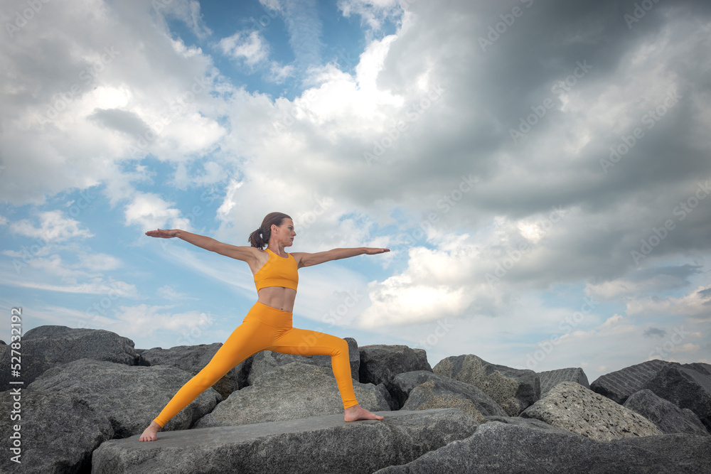 Fit, sporty woman practicing yoga and exercising on rocks outside, warrior pose. Fit, sporty woman practicing yoga and exercising on rocks outside, warrior pose.