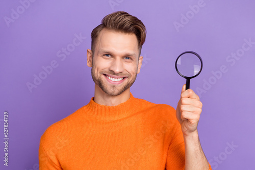 Photo of cheerful positive guy wear orange sweater rising enlarge magnifier isolated violet color background