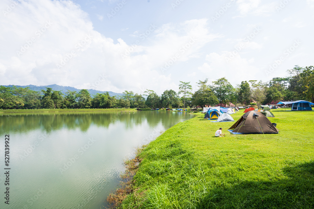 Tourist tents on green grass by the river against a beautiful blue sky.