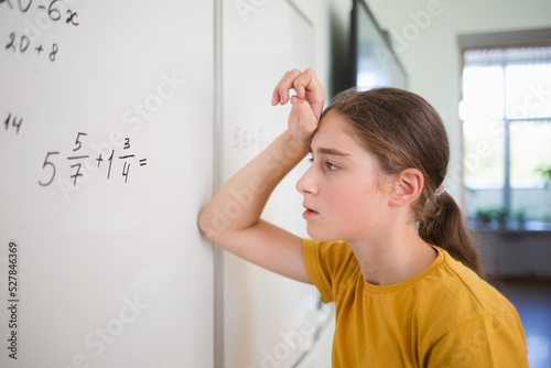 teenager child student thinks over solves example problem with fractions on blackboard in school classroom in math algebra lesson. on face is bright emotion of surprise, difficulty, thoughts
