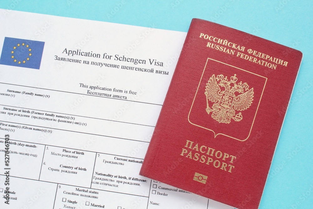 Schengen visa application form in English and Russian language and passport on blue background. Prohibition and suspension of visas for tourists to travel to European Union and Baltic States concept Schengen visa application form in English and Russian language and passport on blue background. Prohibition and suspension of visas for tourists to travel to European Union and Baltic States concept