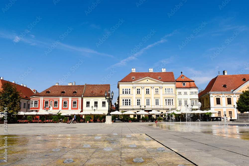 panoramic view of the Szechenyi square in Gyor, Hungary with historic buildings. restaurant terraces at the ground level of residential apartments. blue summer sky. travel and tourism concept. 