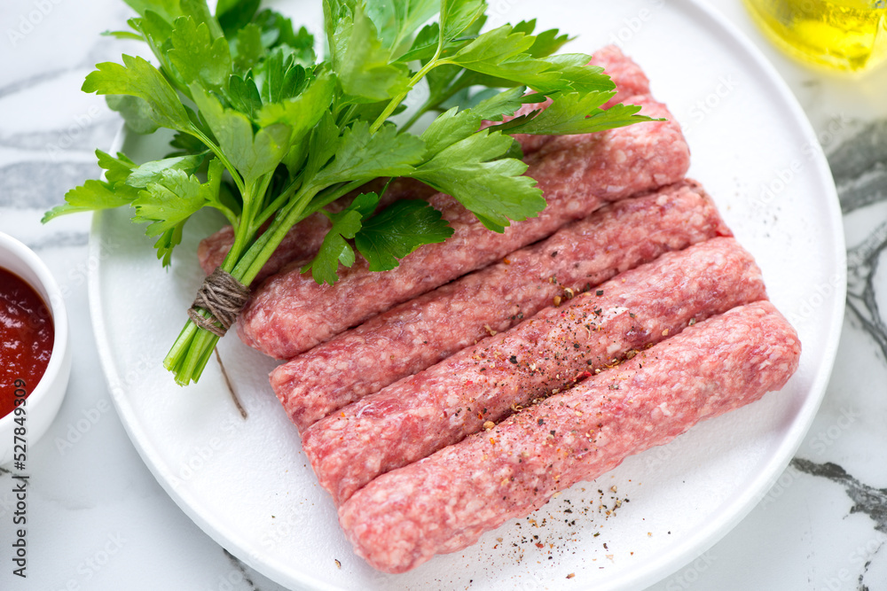 Closeup of raw serbian cevapi or cevapcici sausages with fresh parsley on a white plate, selective focus, horizontal shot