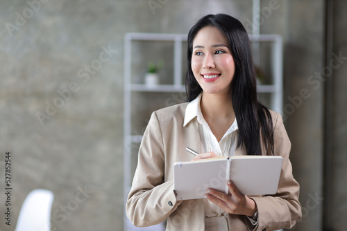 Portrait of a charming business woman in the office standing holding a notepad and pen.