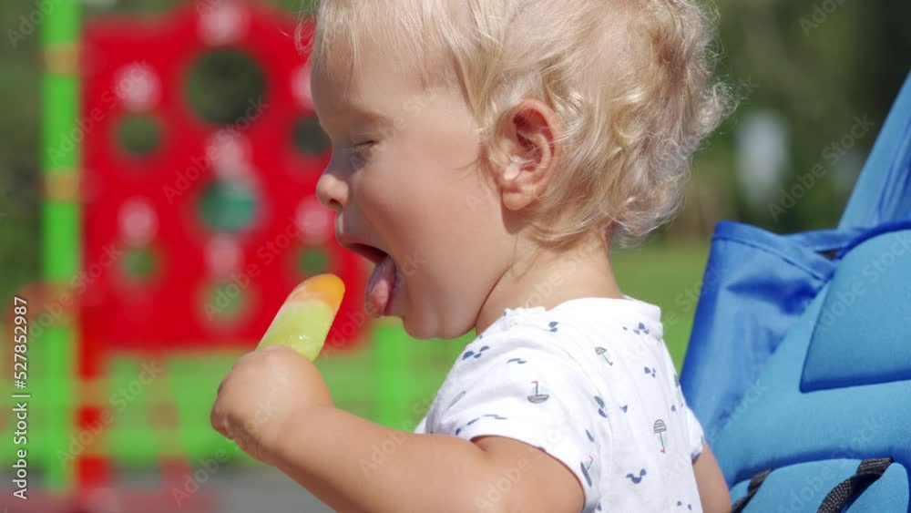 Funny kid making faces while eating popsicle on a summer day, 1.5 year old toddler face closeup.