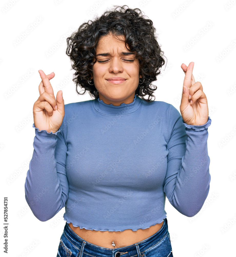 Young hispanic woman with curly hair wearing casual clothes gesturing finger crossed smiling with hope and eyes closed. luck and superstitious concept. Young hispanic woman with curly hair wearing casual clothes gesturing finger crossed smiling with hope and eyes closed. luck and superstitious concept.