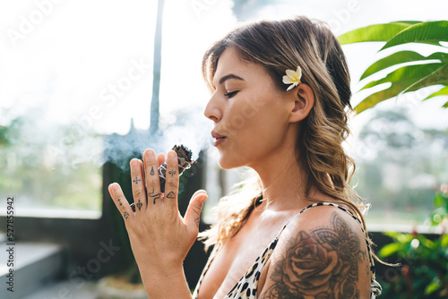 Young woman sniffing and blowing to incense stick photo