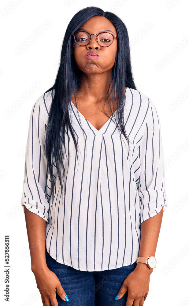 Young african american woman wearing casual clothes and glasses puffing cheeks with funny face. mouth inflated with air, crazy expression. Young african american woman wearing casual clothes and glasses puffing cheeks with funny face. mouth inflated with air, crazy expression.
