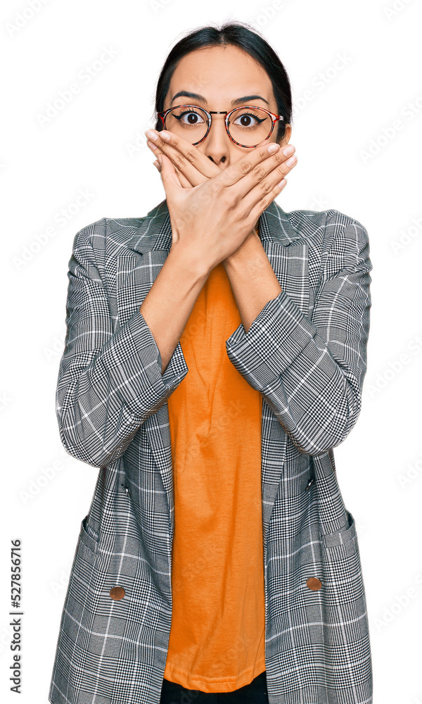 Young hispanic girl wearing business jacket and glasses shocked covering mouth with hands for mistake. secret concept. Young hispanic girl wearing business jacket and glasses shocked covering mouth with hands for mistake. secret concept.