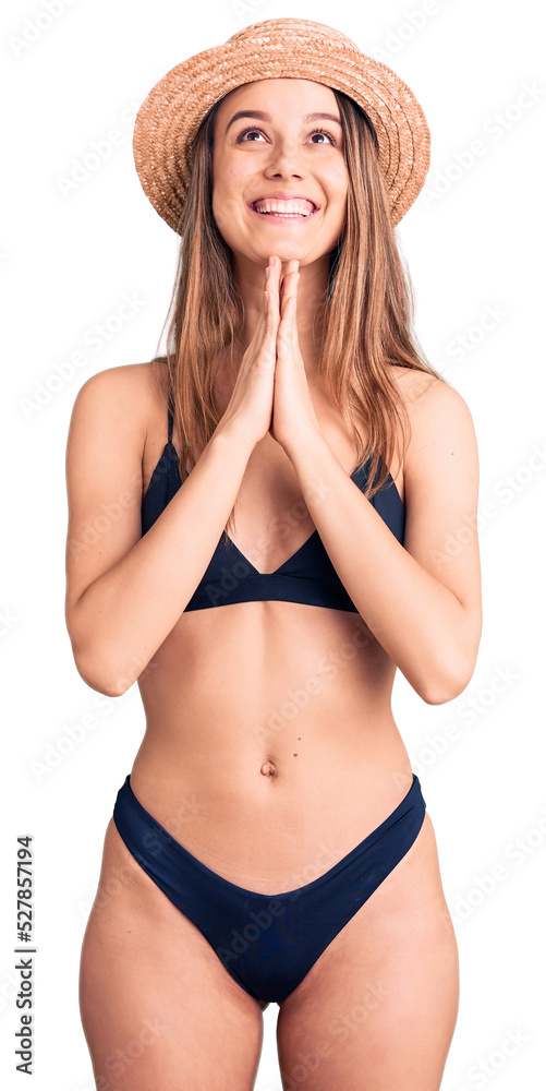 Young beautiful girl wearing bikini and hat begging and praying with hands together with hope expression on face very emotional and worried. begging. Young beautiful girl wearing bikini and hat begging and praying with hands together with hope expression on face very emotional and worried. begging.