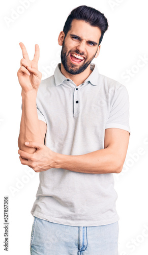 Young handsome man with beard wearing casual polo smiling with happy face winking at the camera doing victory sign. number two.