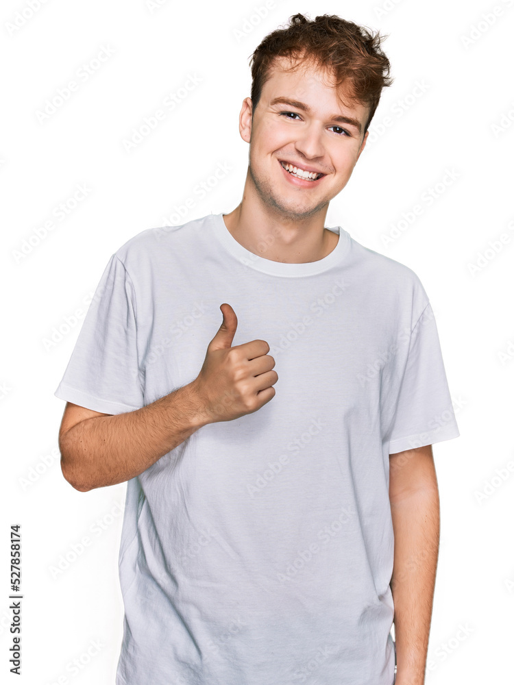 Young caucasian man wearing casual white t shirt doing happy thumbs up gesture with hand. approving expression looking at the camera showing success. Young caucasian man wearing casual white t shirt doing happy thumbs up gesture with hand. approving expression looking at the camera showing success.