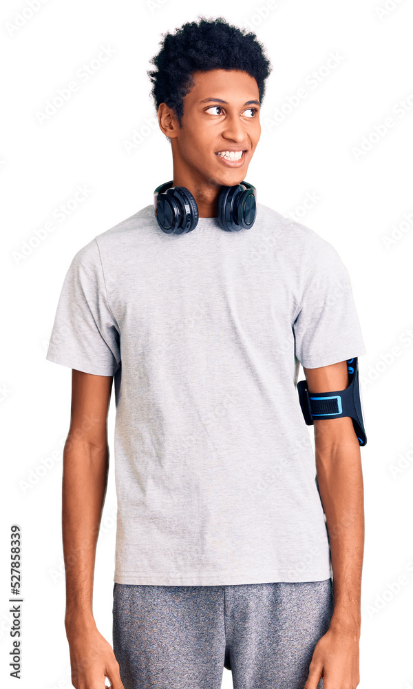 Young african american man wearing gym clothes and using headphones looking away to side with smile on face, natural expression. laughing confident. Young african american man wearing gym clothes and using headphones looking away to side with smile on face, natural expression. laughing confident.