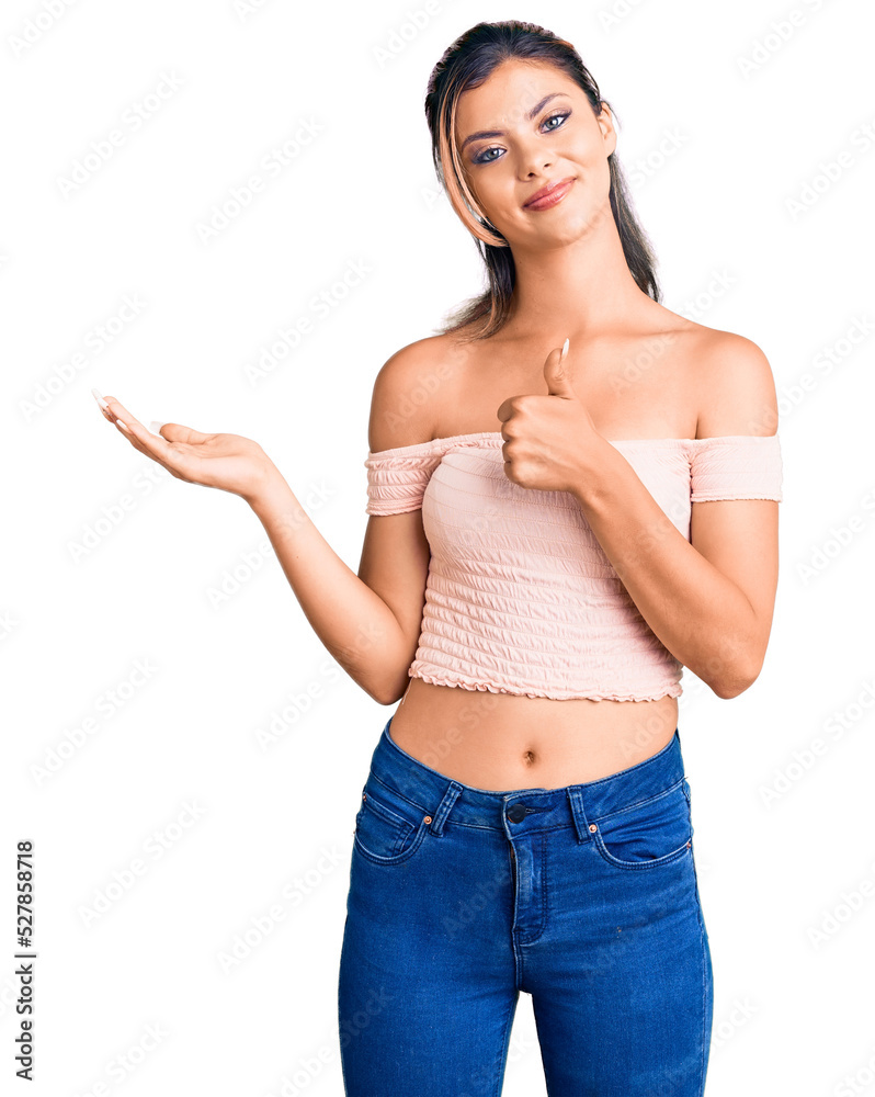 Young beautiful woman wearing casual clothes showing palm hand and doing ok gesture with thumbs up, smiling happy and cheerful Young beautiful woman wearing casual clothes showing palm hand and doing ok gesture with thumbs up, smiling happy and cheerful