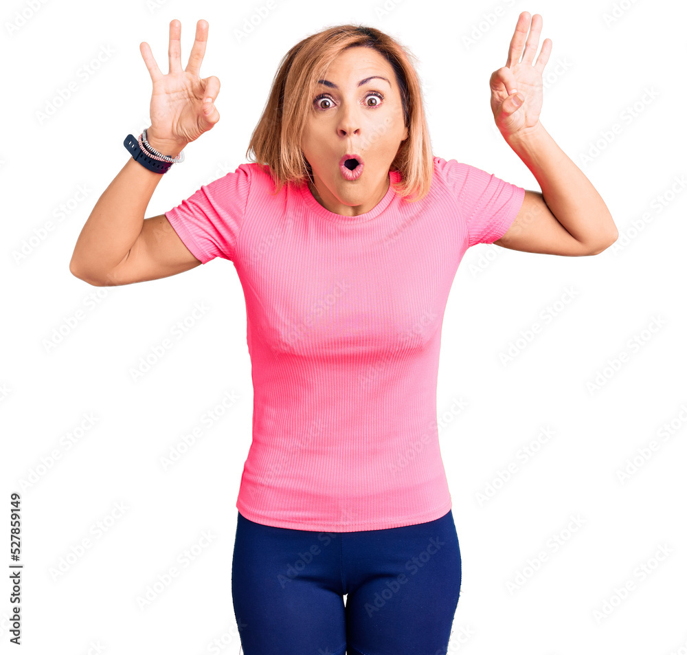 Young blonde woman wearing sportswear looking surprised and shocked doing ok approval symbol with fingers. crazy expression Young blonde woman wearing sportswear looking surprised and shocked doing ok approval symbol with fingers. crazy expression