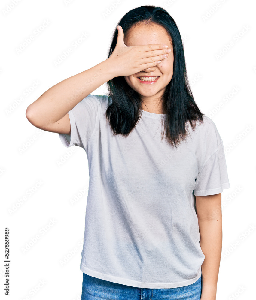 Young chinese woman wearing casual white t shirt smiling and laughing with hand on face covering eyes for surprise. blind concept. Young chinese woman wearing casual white t shirt smiling and laughing with hand on face covering eyes for surprise. blind concept.