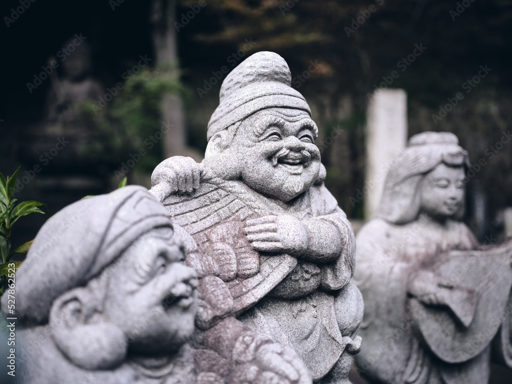 stone statue of laughing Ebisu, one of the japanese seven lucky gods in a quiet temple of tokyo with a dark background stone statue of laughing Ebisu, one of the japanese seven lucky gods in a quiet temple of tokyo with a dark background